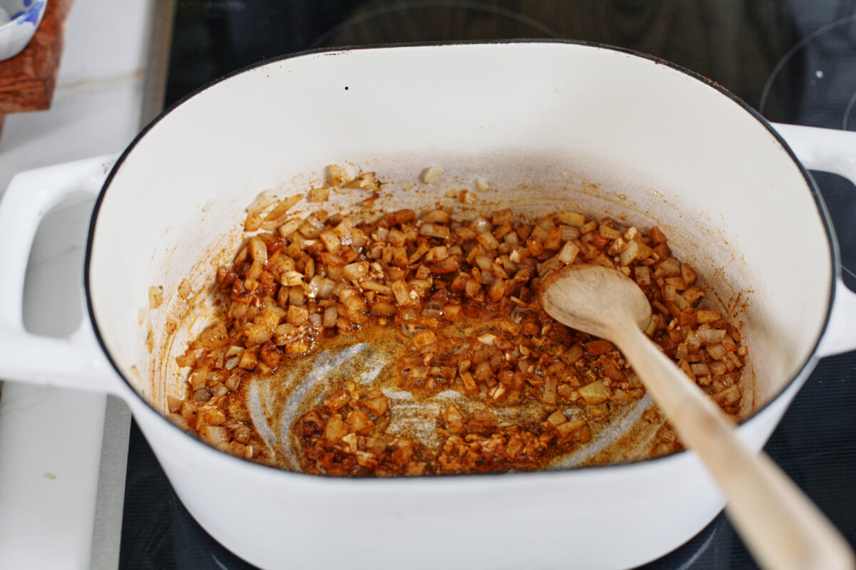 diced onion sautéing with spices in a white dutch oven on the stove