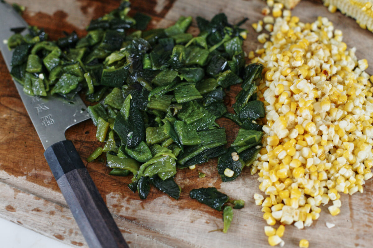 chopped poblano peppers and corn cut off the cobs on a wooden cutting board with a black-handled chef's knife