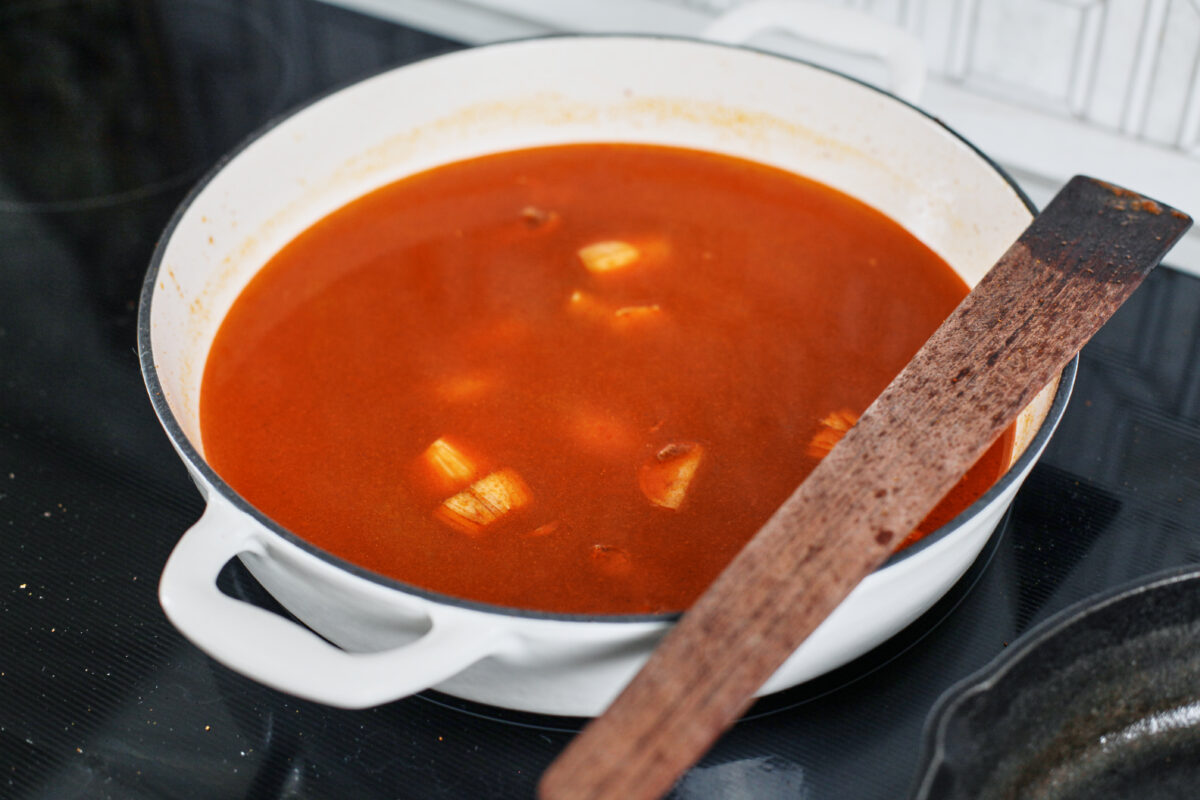 yellow curry broth simmering with aromatics in a large white skillet
