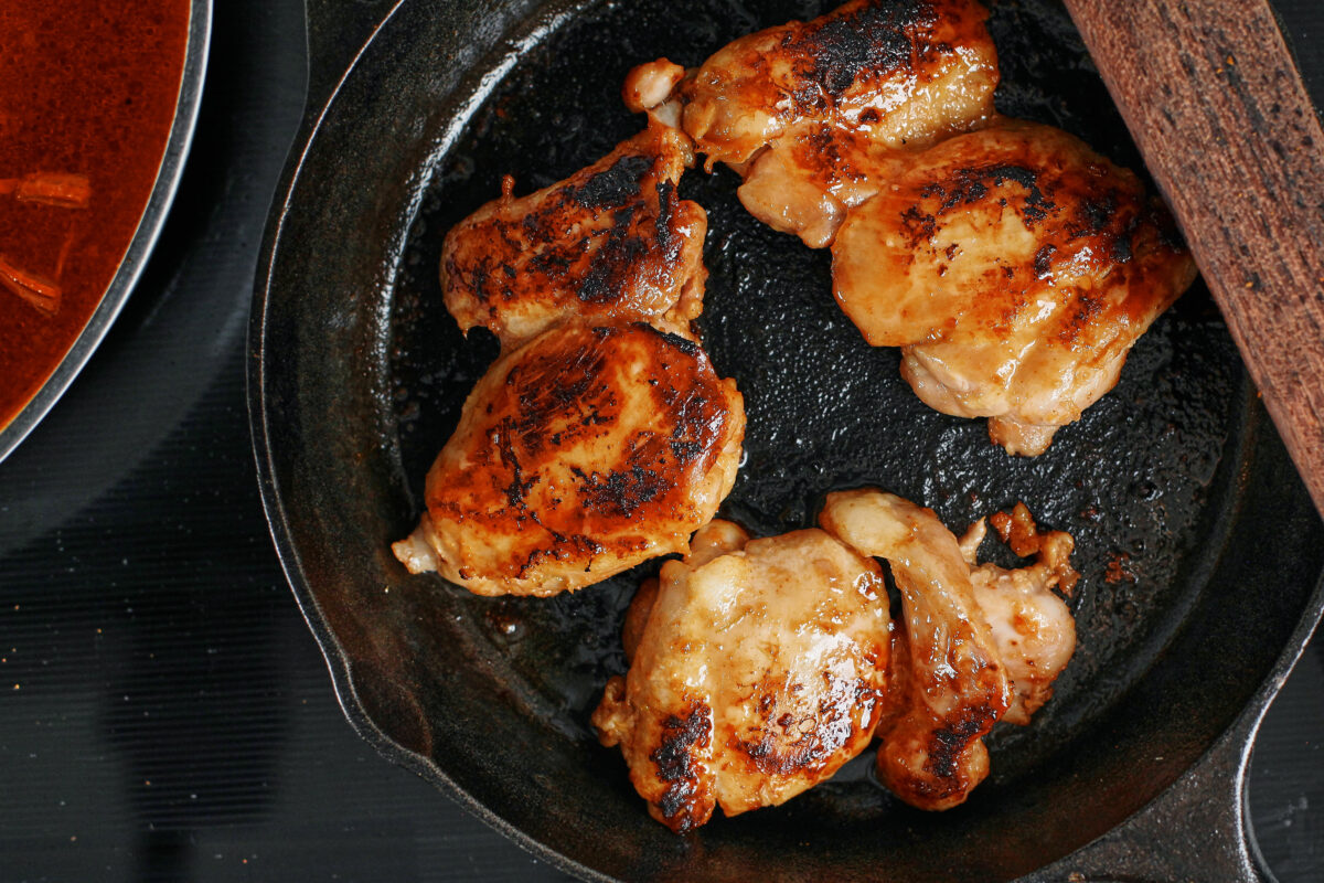 chicken thighs searing in a cast iron skillet