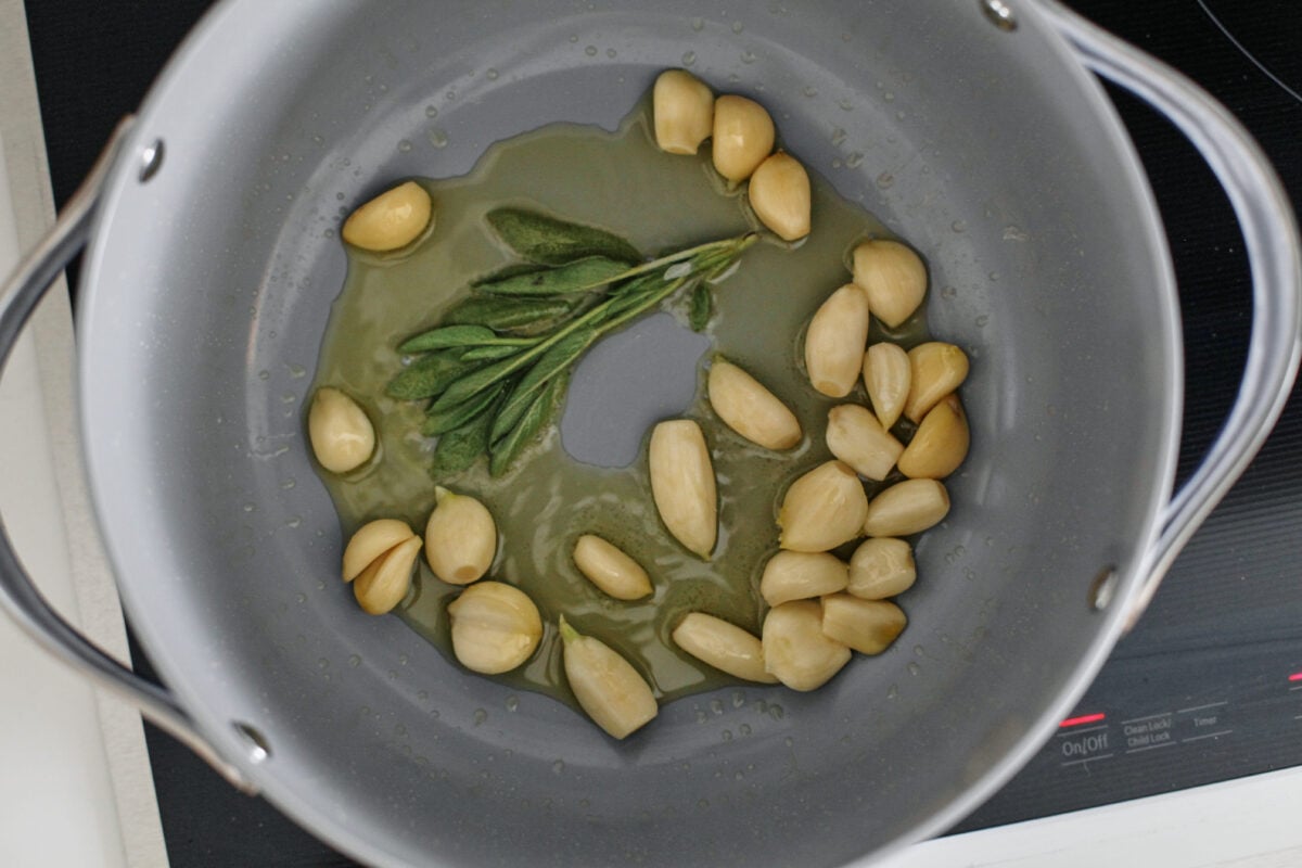 garlic cloves and sage sauteeing in oil in a large opot