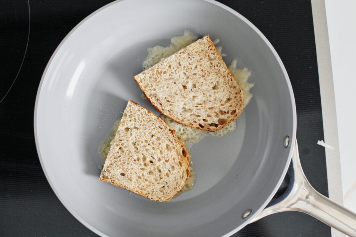 two pieces of cheesy toast melting in a pan