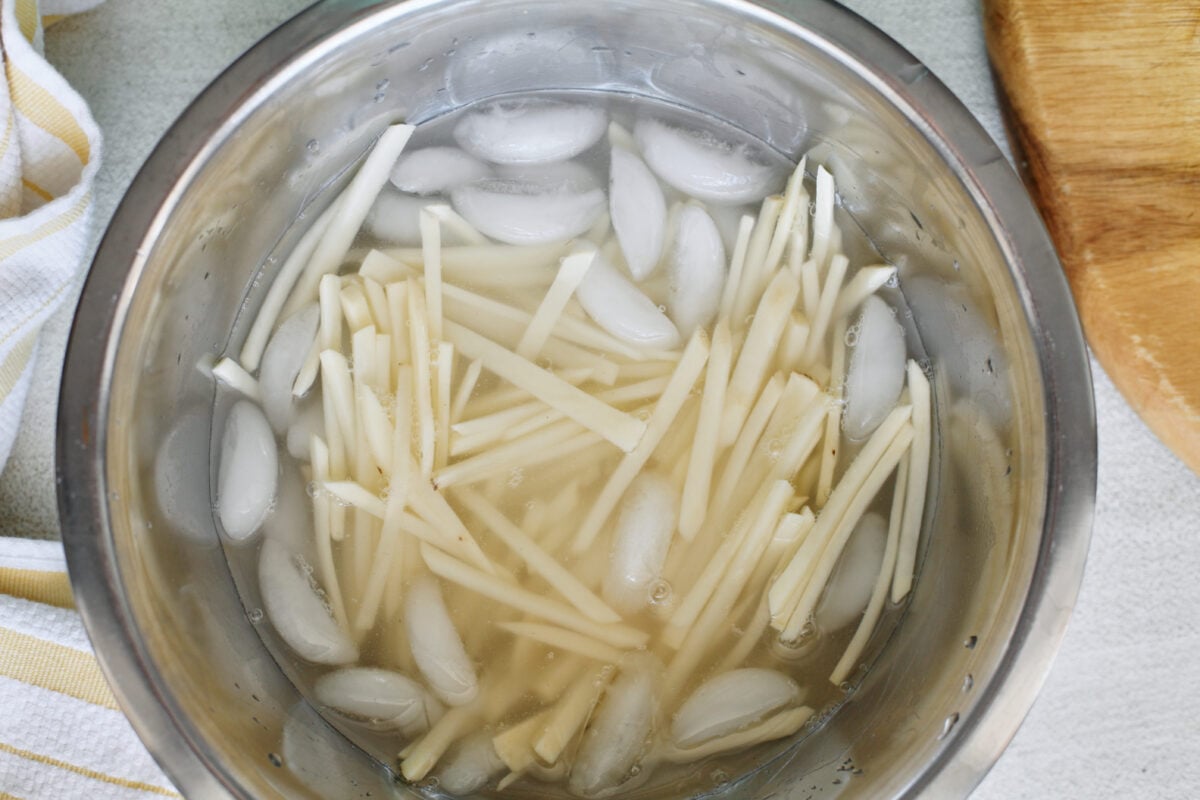 hand cut fries soaking in a large metal bowl of ice water