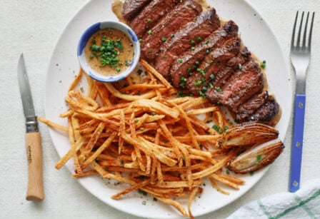 steak frites on a white plate with a small bowl of peppercorn sauce