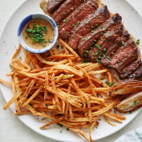 steak frites on a white plate with a small bowl of peppercorn sauce